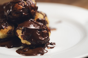 profiteroles covered with black chocolate on plate closeup