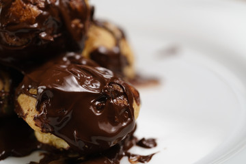 profiteroles covered with black chocolate on plate closeup