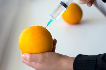Photo of a hand making injection into an orange on a light background