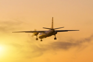 Naklejka na ściany i meble Airplane landing against the backdrop of the sunset sun.