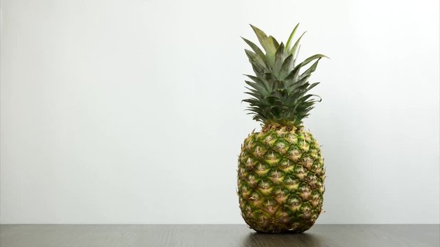 Pineapple appears in the frame, spinning and leaving the frame. One pineapple rotating on the desk on white background. Stop motion