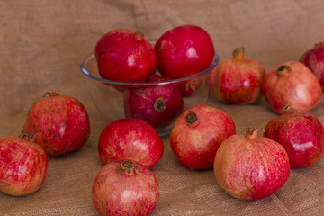 Naklejka na ściany i meble Ripe red pomegranates in a glass bowl on a brown burlap