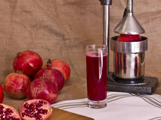 Pomegranate juice in a glass next to a cut pomergranat on a board. Metal juicer press behind.