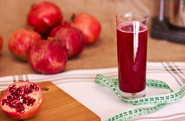 Pomegranate juice in a glass with meter tape next to a cut pomergranat on a board. Metal juicer press behind.