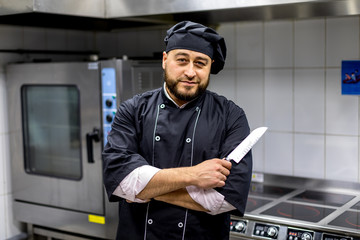 Chef in the kitchen.black uniform chef keeps a knife in his hand