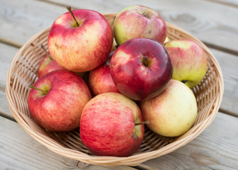 Fresh red yellow apples  in wicker plate on wooden table. Concept for seasonal fruits, autumn harvest and agriculture.