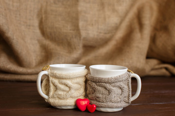 Love background, two cups of coffee with knitted cup holder near two hearts for valentine's day. Copy space for love text	