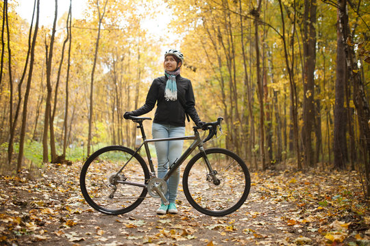 Image of girl in helmet, jeans next to bicycle in autumn park