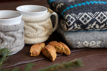 Fototapeta na wymiar Winter morning, cups of coffee with knitted cup holders near knitted sweater and cake. Ideal for winter couple in love 