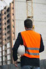 worker or engineer holding in hands helmet for workers security on background of new highrise apartment buildings