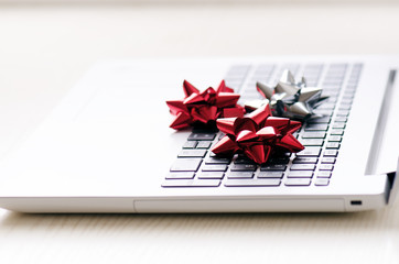 Christmas decoration on a computer. Red and silver ribbon on laptop desktop. Computer on a wooden table and white wall. Business concept during a holiday. Xmas concept. 