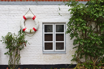 Whitewashed brick wall with window, green bushes and red and white life buoy