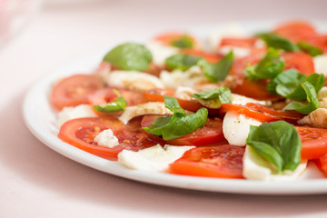 Tomato and mozzarella salad with basil leaves, sprinkled with pepper, olive oil and acceto balsamico on the white plate