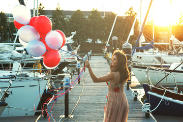 Woman in beautiful dress with a lot of colorful balloons on the yacht pier