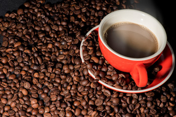 Hot coffee in red cup and coffee beans are the background.