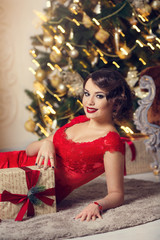 Happy Brunette woman in red dress with gift boxes in luxury interior. Christmas tree. New Year decorations.