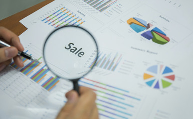 Magnifying glass on "Sale" text on chart on the desk, finance and investment concept.