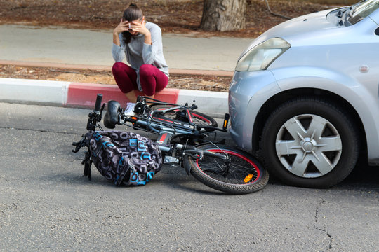 A woman holding her head near a traffic accident between electric bicycle and car