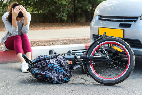 A woman holding her head near a traffic accident between electric bicycle and car