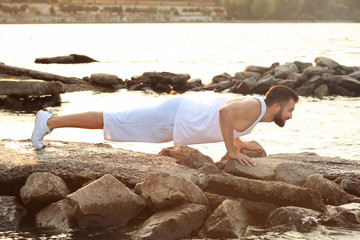 Handsome young man exercising on river bank