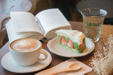 Top view of coffee cup and green tea cake , smart phone , book , on table in coffee shop relax time