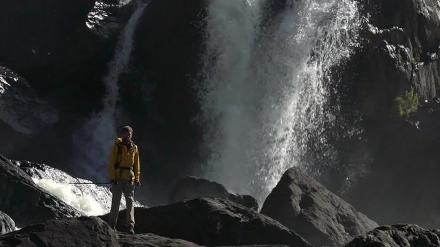 A male hiker walks at a waterfall in slow motion.