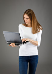 Naklejka premium Young woman standing with laptop on gray background
