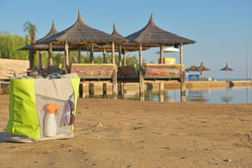 beach bag with sunscreen and sunglasses on the beach by the sea