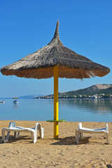 Straw beach umbrella and two white sunbed