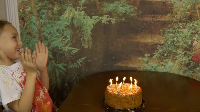Funny girl can not blow birthday candles on cake. Joke party at home. Young girl blowing candles on cake. Lot of smoke and ash on table. Fast motion effect. Girl clapping.