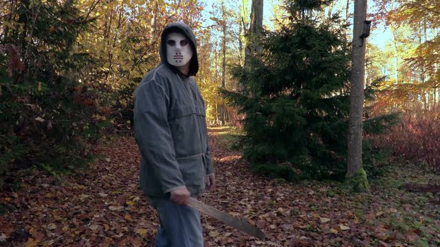 Man with Halloween mask and machete alone on path in park