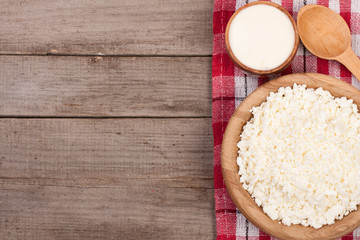 Cottage cheese in a wooden bowl with sour cream on old wooden background with copy space for your text. Top view