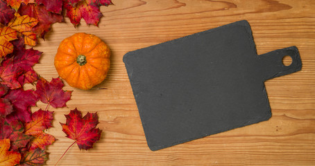 Herbstlaub mit Kürbis auf einem Holzbrett mit Schiefertafel