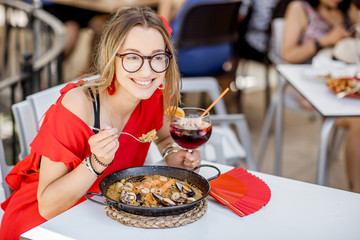 Young woman in red dress eating sea Paella, traditional Valencian rice dish, sitting outdoors at...