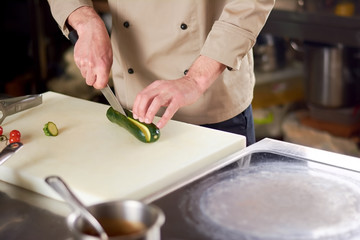 Male chef cutting green zucchini. Zucchini being chopped on white cutting board by male chef. Chef cutting vegetables on cutting board.