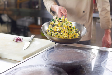 Chef holding frying pan with sliced vegetables. Chef is stirring sliced vegetables in frying pan at professional kitchen. Preparation of european food.