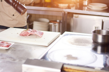 Chef processing ribs with spices. Male chef preparing pork ribs at professional kitchen. European delicious food.