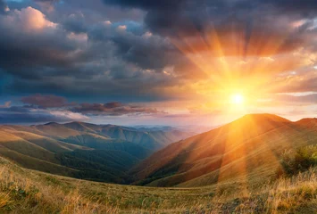 Papier Peint photo Lavable Ciel Panoramic landscape of fantastic sunset in the mountains. View of the autumn hills lit by the rays of the evening sun. Dramatic clouds over sky.