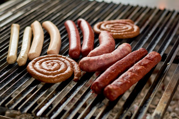 Sausages assortment grilling on metal grill. Assorted delicious grilled meat over the coals on a barbecue.