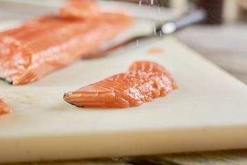 Sprinkling of salt on raw salmon. Fresh piece of salmon on cutting board, cooking process.