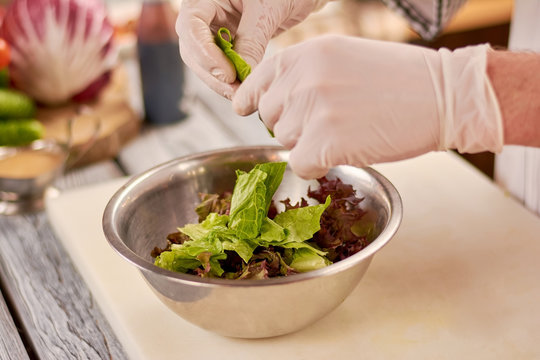 Chef hands chopping lettuce leaves. Green and purple lettuce leaves in stainless bowl. Chef at work, kitchen.