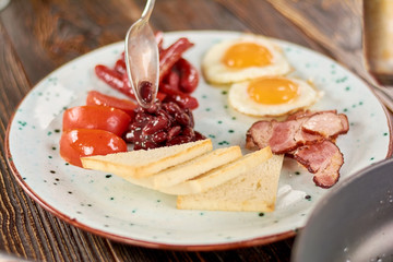 Full english breakfast on plate. Chef putting beans on plate with english breakfast. English breakfast in restaurant.