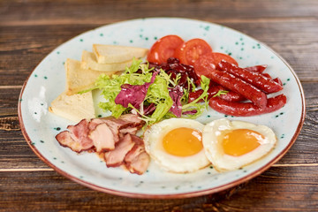 English breakfast with fresh salad. English breakfast - fried eggs, baked bacon and sausages, toasts, tomatoes and green salad. Appetizing dish on plate.