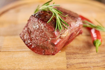 Appetizing grilled beef steak. Beef steak medium grilled with rosemary and red chili pepper. Delicious food on wooden background.