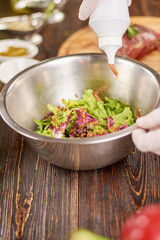 Mixed salad is pouring with mustard. The process of cooking green salad at professinal kitchen. Healthy and delicious food.