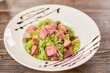 Green salad with beef, cornichons and mustard. Appetizing and healthy salad in restaurant. Delicious dinner on plate.