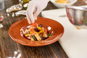 Chef hand sprinkling salt on salad. Appetizing salad with roasted chicken and grilled vegetables. Chef cooking delicious food at kitchen.