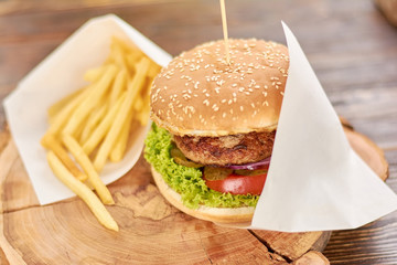 Burger with fried potatoes on wood. Classic american food - burger. Appetizing burger with fresh vegetbles, meat and french fries.