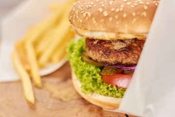 Appetizing fresh burger close up. Delicious burger with meat, lettuce, tomatoes, cheese, pickled cucumber close up. Classsic american food.