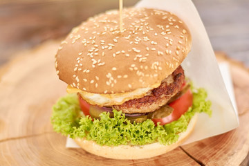 Fresh hamburger on wooden background. Close up of fresh appetizing burger with cutlet, cheese, onion, tomato, cucumbers, lettuce. Traditional american food.